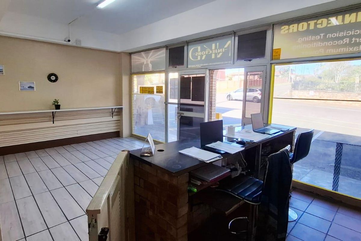 Commercial office space featuring a built-in brick reception counter, large street-facing glass windows, and tiled flooring, suitable for a retail or service-based business.