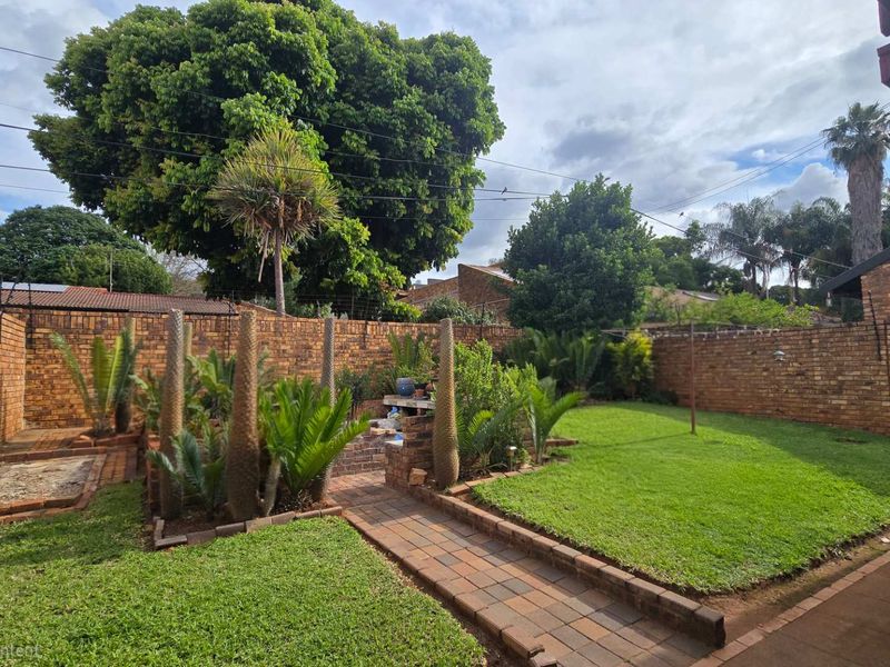 A private rear garden featuring a well-maintained lawn, paved pathway, and a built-in brick braai area enclosed by high brick boundary walls.