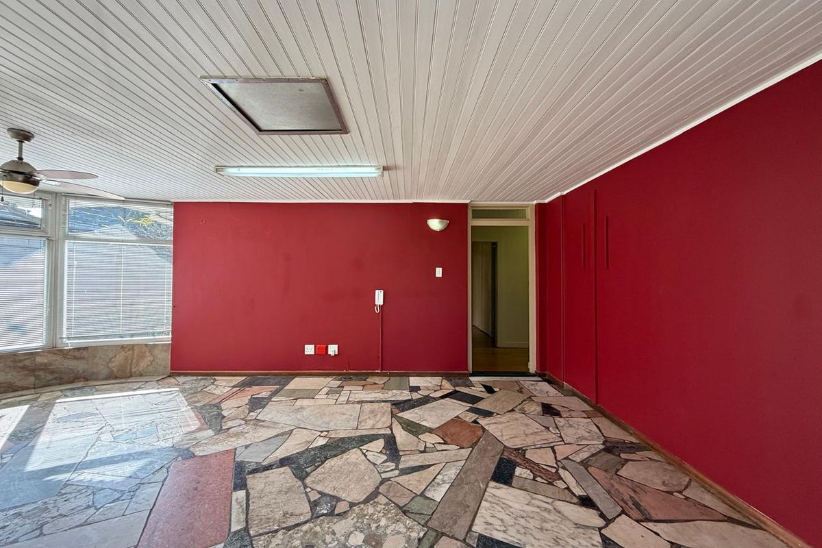 An empty office space featuring distinctive stone mosaic flooring, red accent walls, and a white paneled ceiling with integrated lighting.