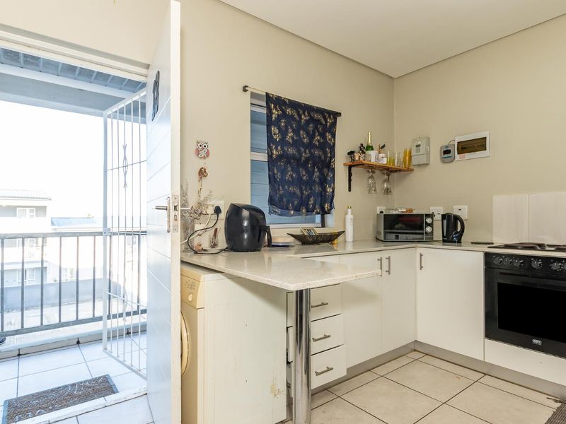 Compact kitchen featuring white cabinetry, stone countertops, built-in oven and hob, with direct access to a private balcony.