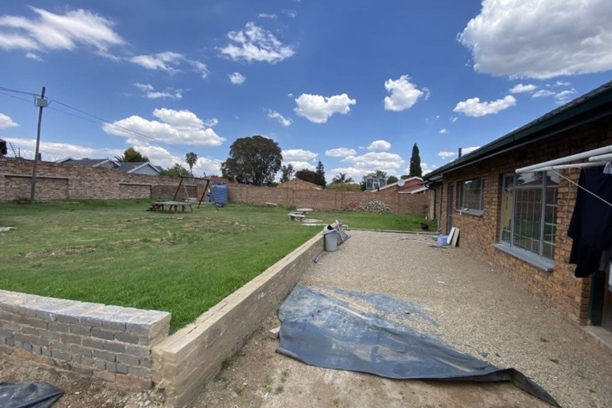 Spacious rear garden featuring a brick boundary wall, a gravel patio area, and an expansive lawn, offering significant potential for landscaping and outdoor improvement.