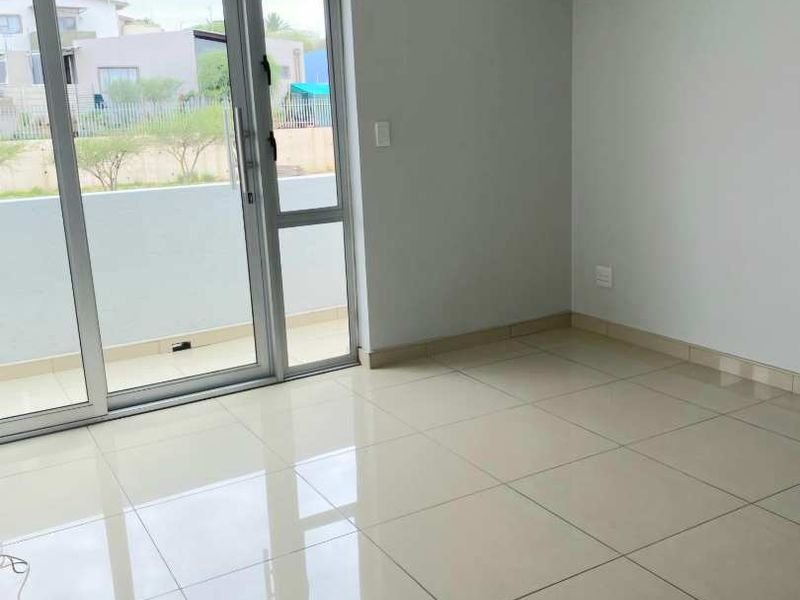 A bright, empty living area featuring large format floor tiles, a sliding glass door leading to a balcony, and modern clerestory windows.