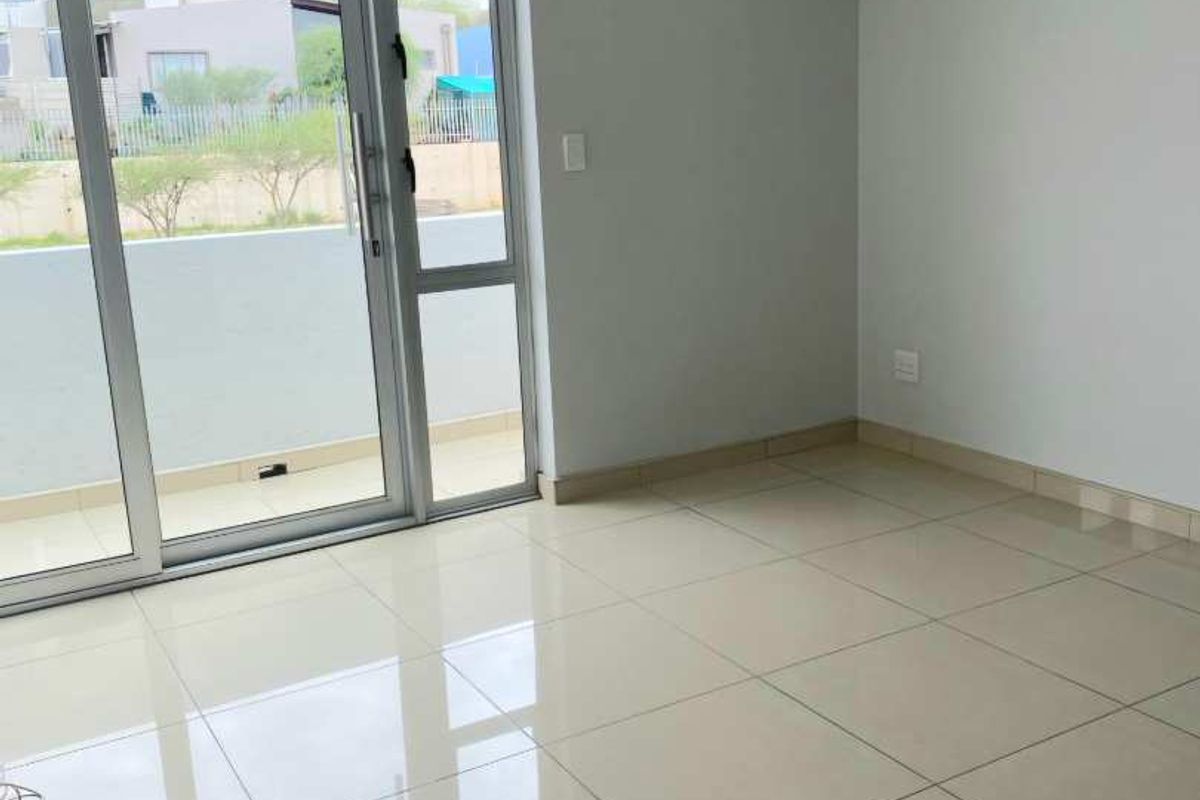 A bright, empty living area featuring large format floor tiles, a sliding glass door leading to a balcony, and modern clerestory windows.