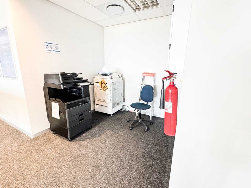 A functional utility or storage space featuring carpeted flooring, a suspended ceiling with recessed lighting, and a wall-mounted fire extinguisher.