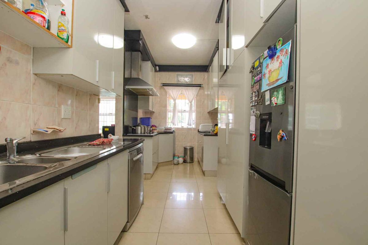 A galley-style kitchen featuring high-gloss cabinetry, dark stone countertops, a stainless steel sink, and an integrated extractor fan.