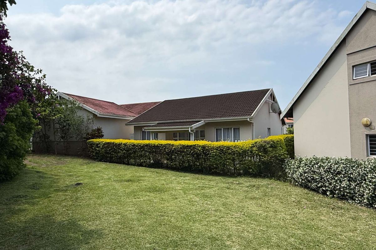 A view of the rear exterior of the residential property, featuring a well-maintained lawn, landscaped hedges, and tiled roof structures.