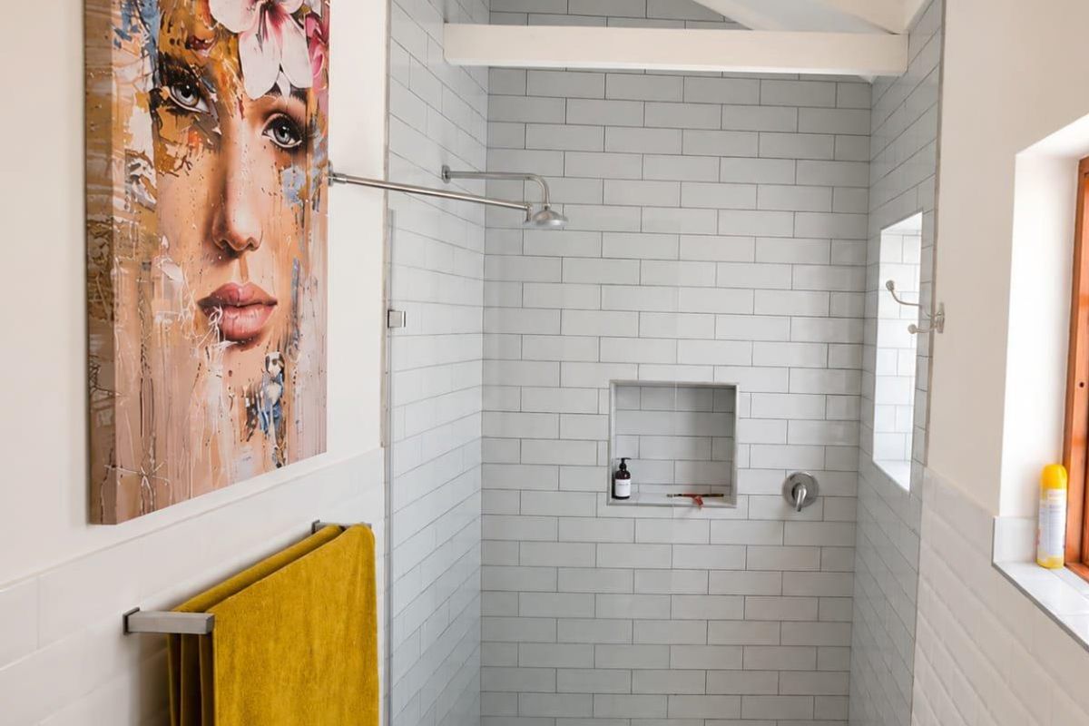 Modern bathroom featuring a walk-in shower with light grey subway tiles, a recessed niche, and a pebble mosaic floor under exposed ceiling beams.