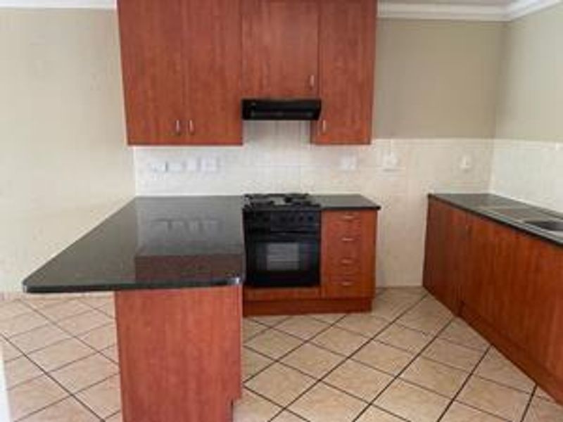 A functional kitchen featuring dark granite countertops, built-in cabinetry, a gas hob with extractor fan, and tiled flooring throughout.