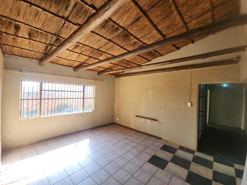An empty living area featuring a traditional thatched ceiling with exposed timber beams, tiled flooring, and security bars on the window.