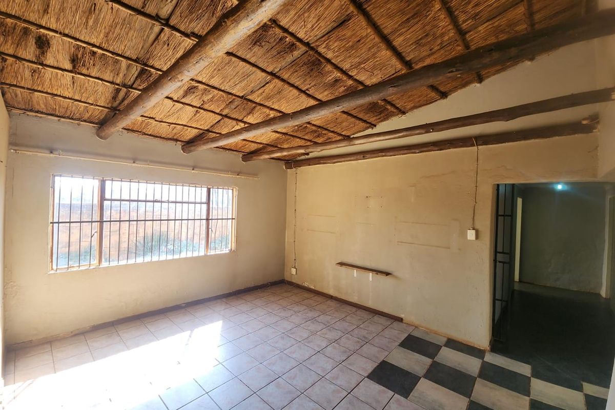An empty living area featuring a traditional thatched ceiling with exposed timber beams, tiled flooring, and security bars on the window.