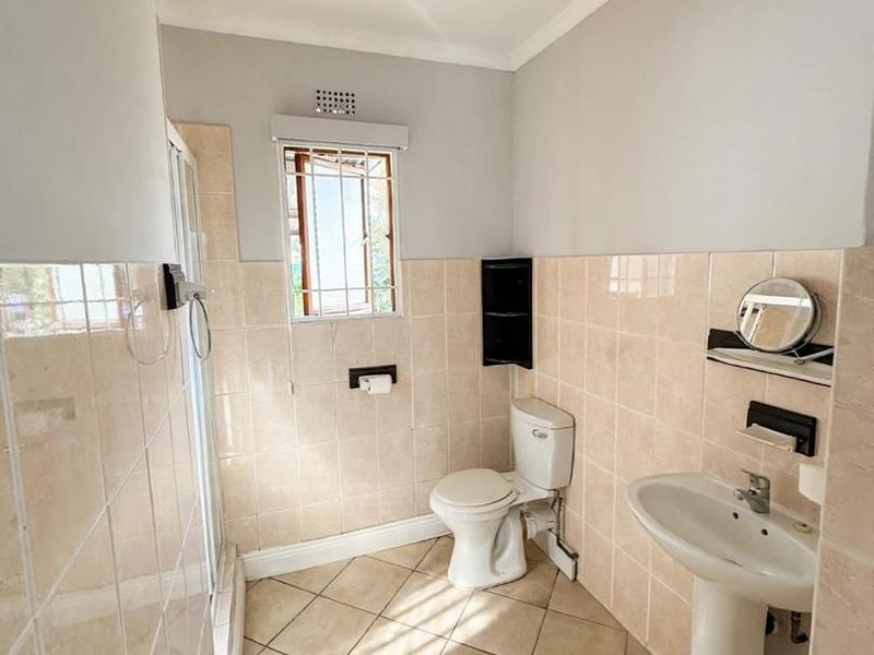 A functional bathroom featuring a pedestal basin, toilet, and shower enclosure with neutral ceramic tiling throughout.