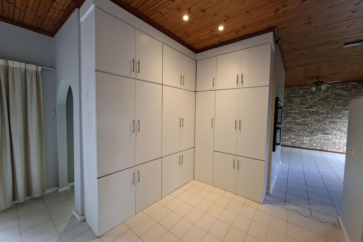 A spacious kitchen area featuring extensive built-in white cabinetry, tiled flooring, and a distinctive timber-paneled ceiling with recessed lighting.