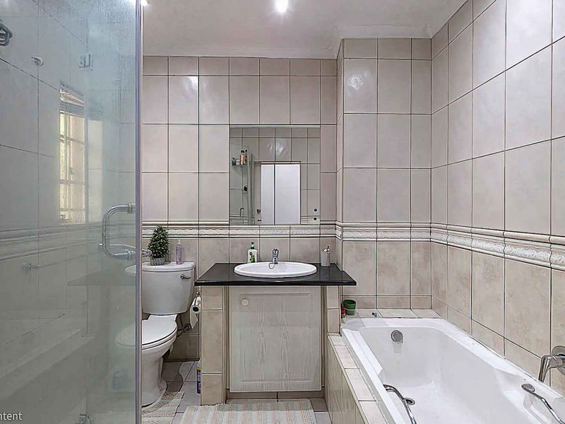 A functional bathroom featuring a built-in vanity with a basin, a separate bathtub, and a glass-enclosed shower with neutral wall tiling.