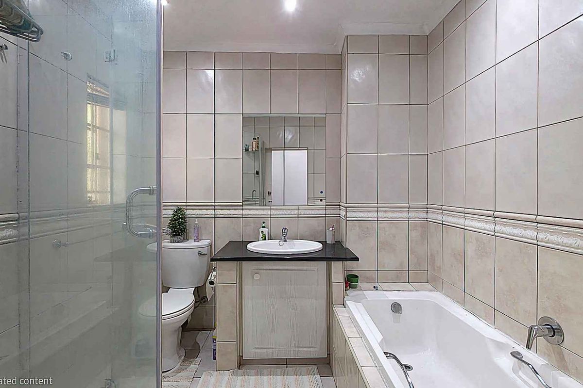 A functional bathroom featuring a built-in vanity with a basin, a separate bathtub, and a glass-enclosed shower with neutral wall tiling.