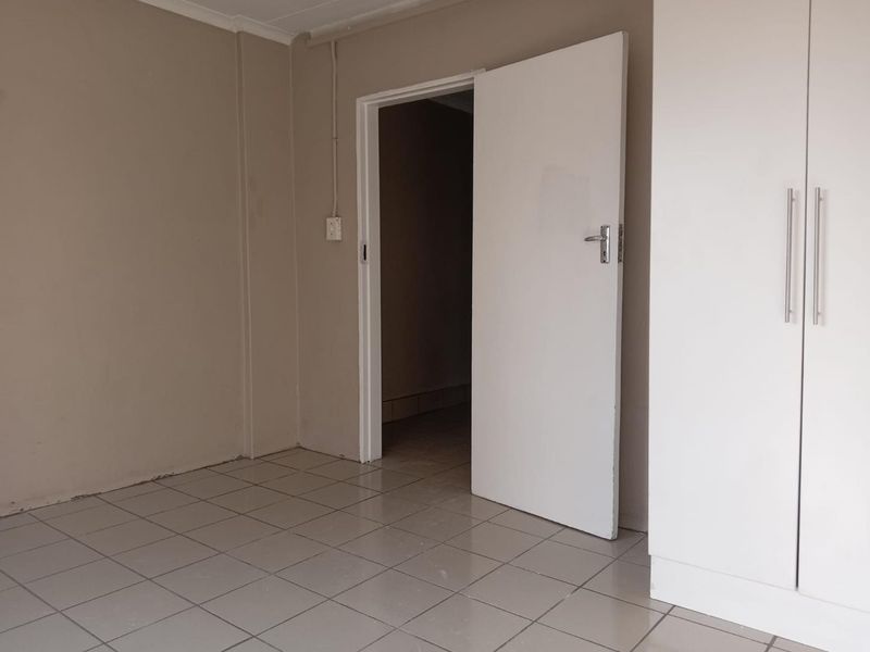 An empty bedroom featuring neutral wall paint, tiled flooring, and built-in cupboards with modern handles.