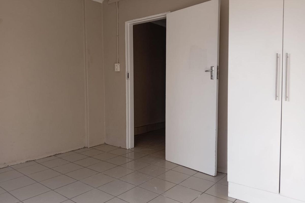 An empty bedroom featuring neutral wall paint, tiled flooring, and built-in cupboards with modern handles.
