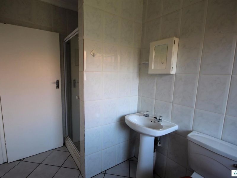 A functional bathroom featuring a pedestal basin, a shower enclosure, and a toilet, finished with neutral ceramic wall and floor tiles.