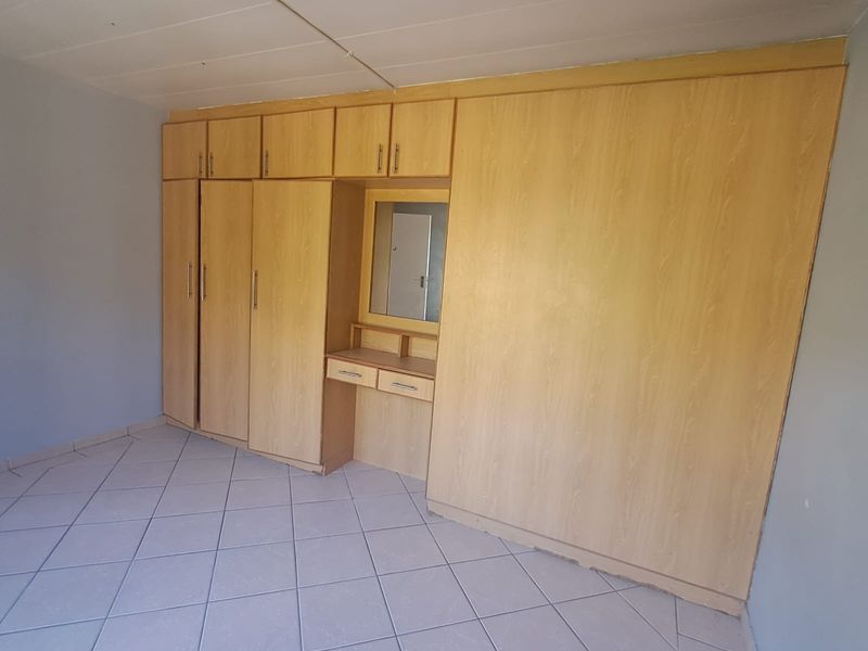 A bedroom featuring extensive built-in wooden cupboards with an integrated vanity mirror and tiled flooring.