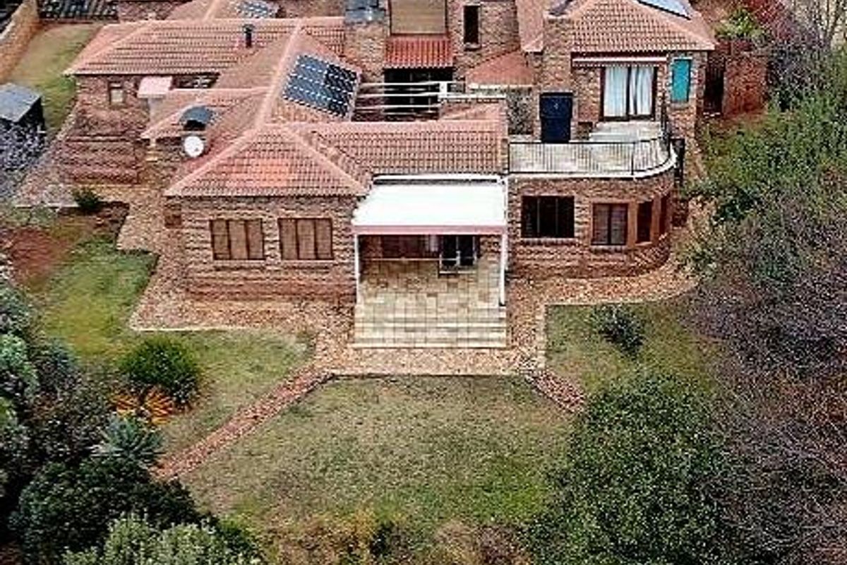 Aerial view of a large brick house featuring a tiled roof, solar panels, a covered patio, and a spacious garden.