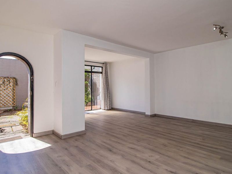 A bright, empty living room featuring modern laminate flooring, an arched entrance, and a sliding glass door providing access to a private outdoor area.