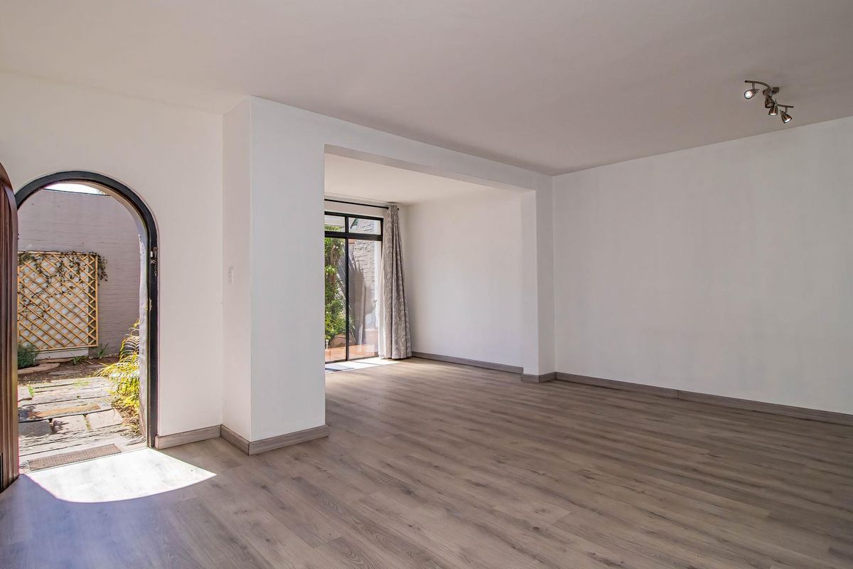 A bright, empty living room featuring modern laminate flooring, an arched entrance, and a sliding glass door providing access to a private outdoor area.