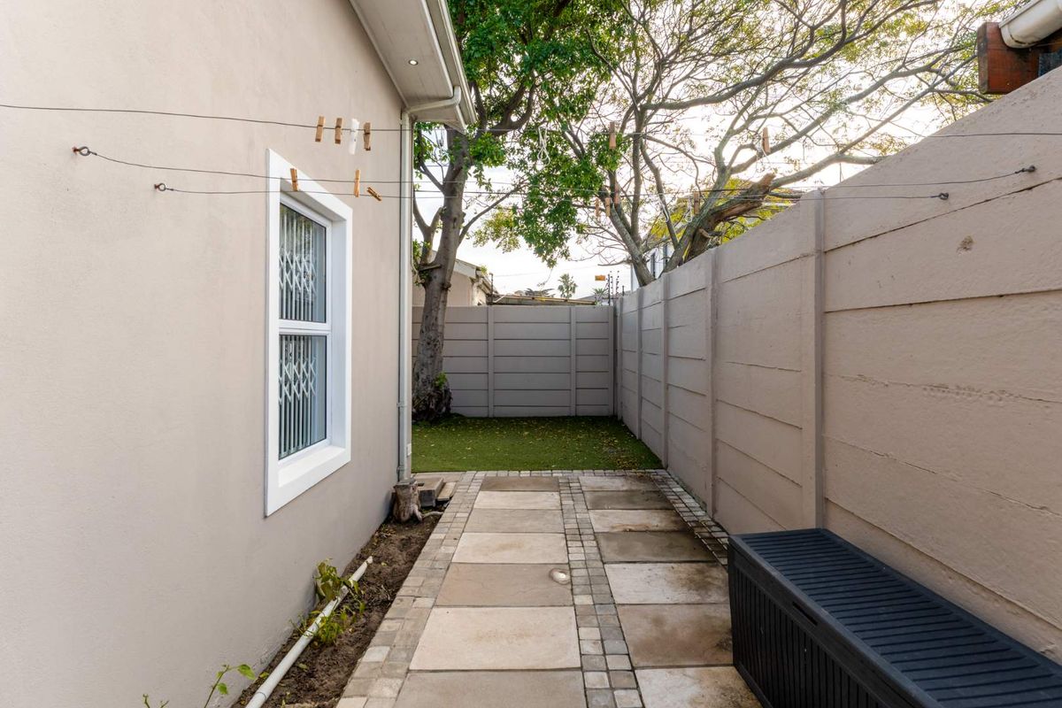 A side exterior area featuring paved walkways, a small patch of artificial lawn, and perimeter boundary walls.