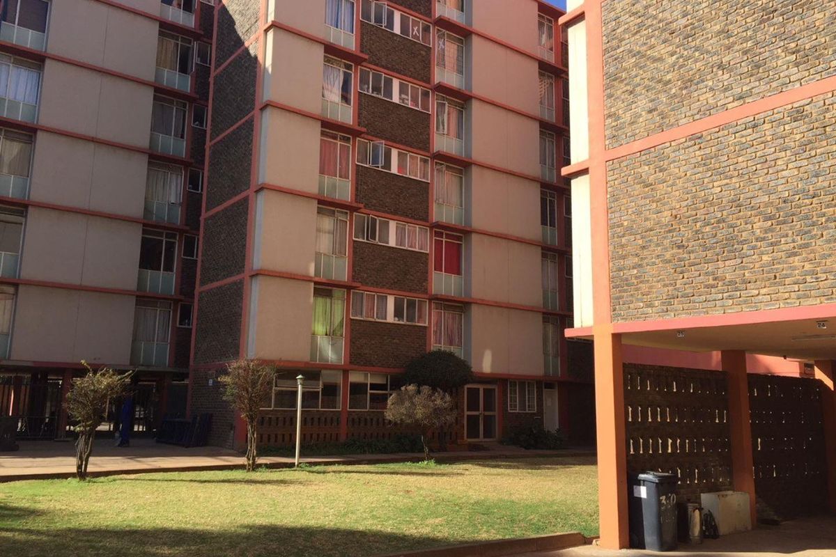 Exterior view of a multi-story apartment complex featuring brick and concrete facade with a shared communal garden area.