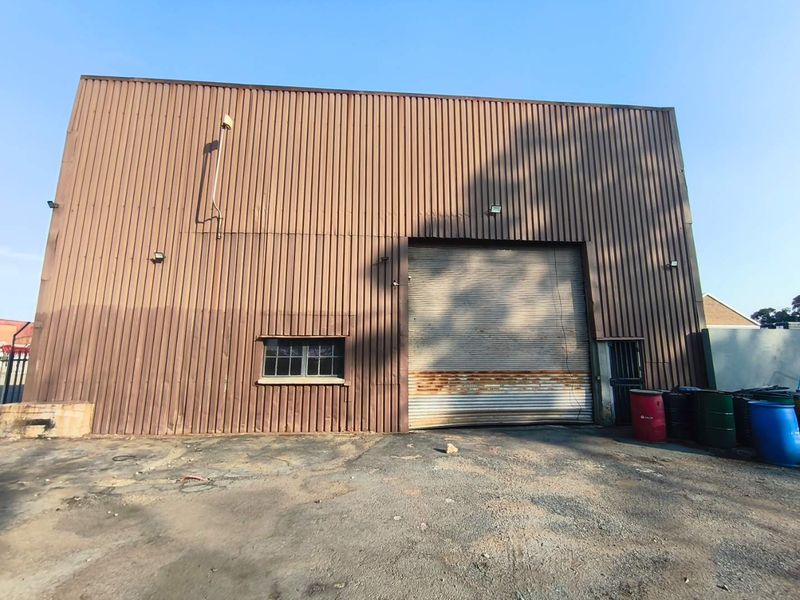 Rear elevation of an industrial warehouse featuring corrugated metal cladding and a large roller shutter door with visible surface corrosion.