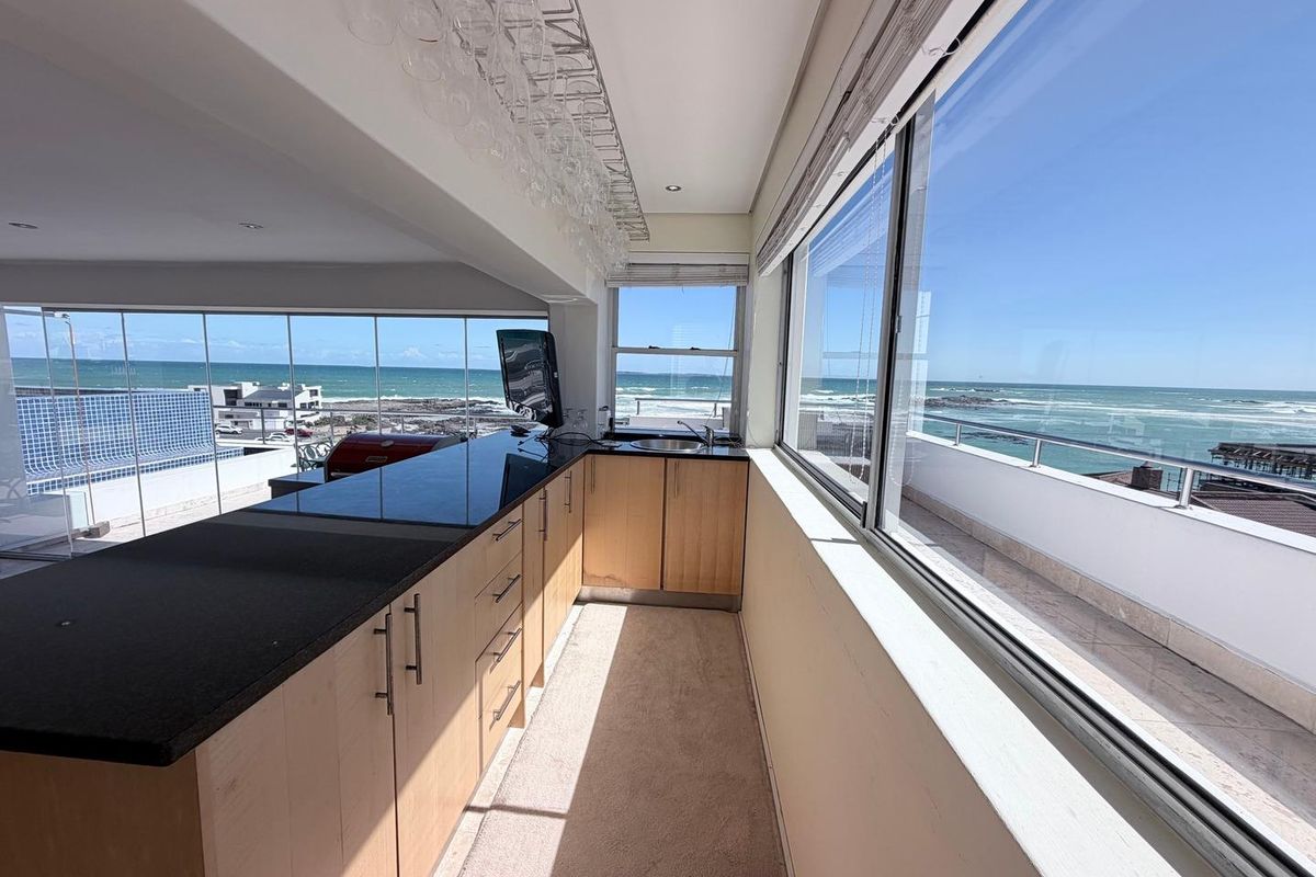 Modern kitchen area featuring granite countertops, built-in cabinetry, and expansive windows offering panoramic ocean views.