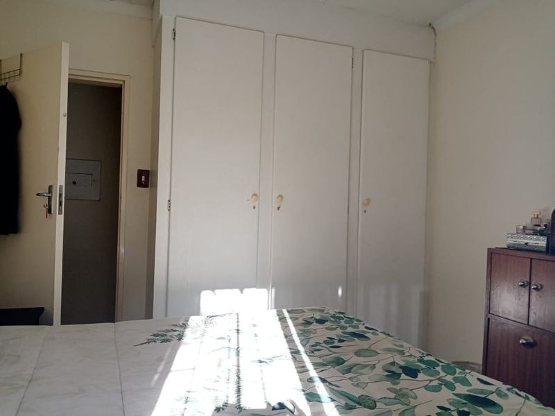 A bedroom featuring built-in cupboards and access to an adjoining room, offering a functional space with potential for cosmetic updates.
