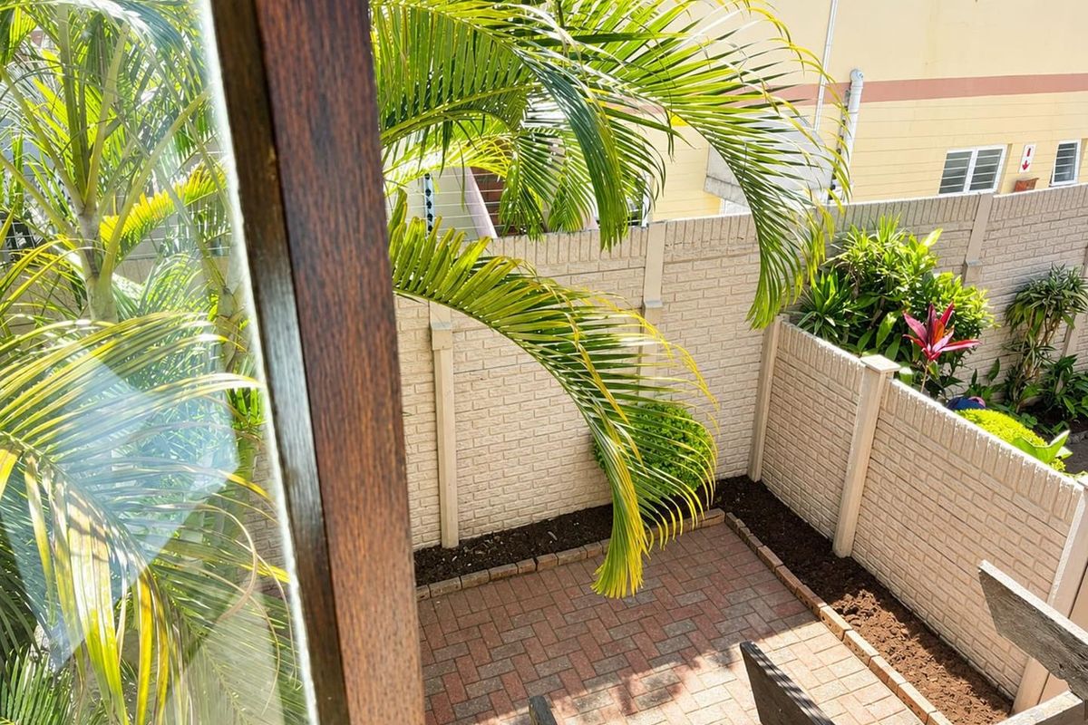 A private rear courtyard featuring brick paving, established garden beds, and secure precast concrete boundary walls, viewed from an elevated position.
