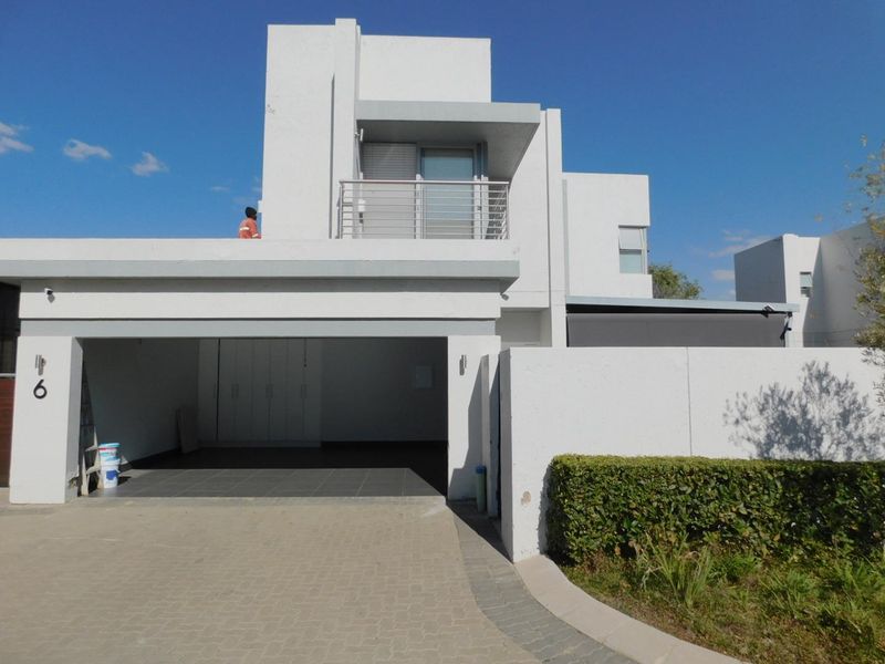 Modern cluster home exterior featuring a double garage, paved driveway, and an upper-level balcony with clean architectural lines.