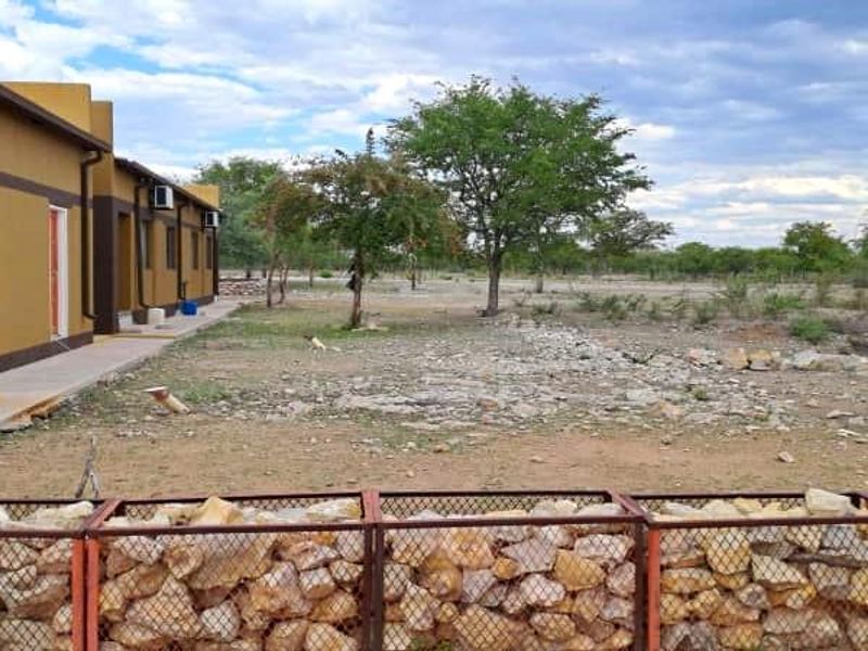 Rear exterior view of the farm building featuring a concrete walkway, wall-mounted air conditioning units, and a stone-filled gabion boundary fence.