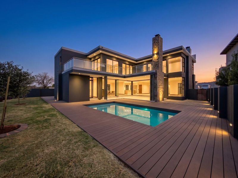 Modern double-story residence featuring a swimming pool, expansive composite decking, stone-clad chimney, and large glass sliding doors opening to the rear garden.