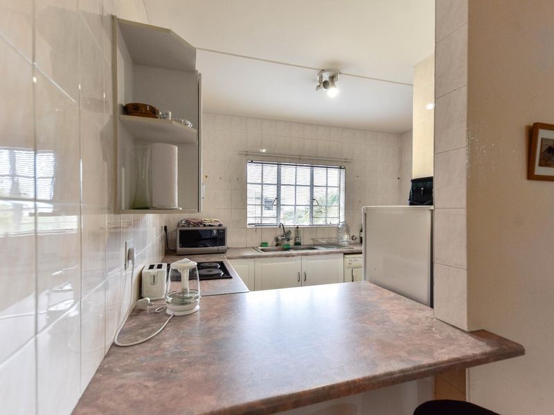 A functional kitchen featuring laminate countertops, tiled splashbacks, built-in cabinetry, and a stainless steel sink, offering a practical layout for daily use.