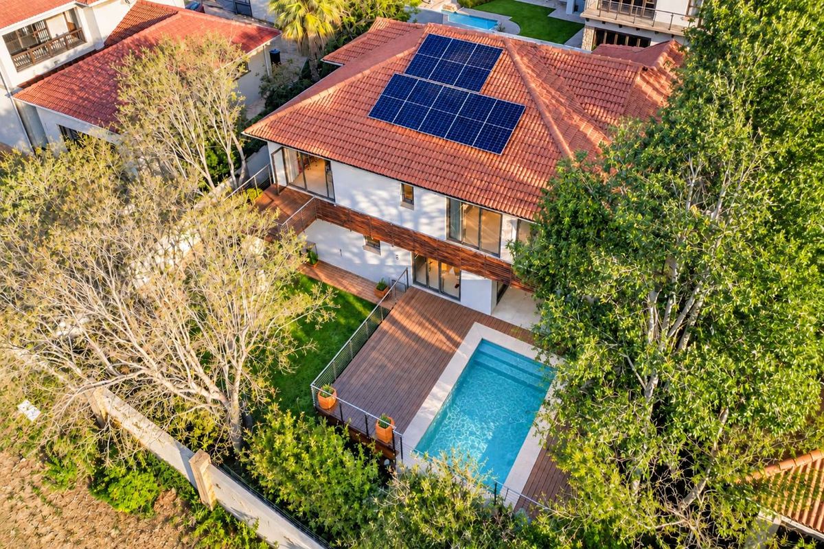 Aerial view of a residential property featuring a tiled roof with solar panels, a swimming pool, timber decking, and a well-maintained garden.