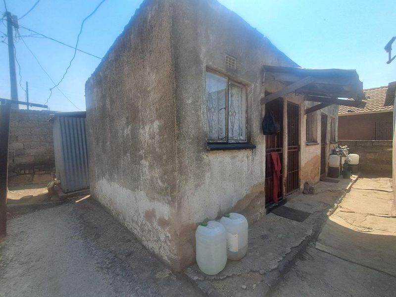Rear view of a small residential structure showing significant exterior wall weathering and basic security features.