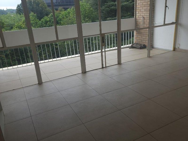 An enclosed balcony featuring tiled flooring, large glass panels, and a metal balustrade, offering an open space ready for customization.