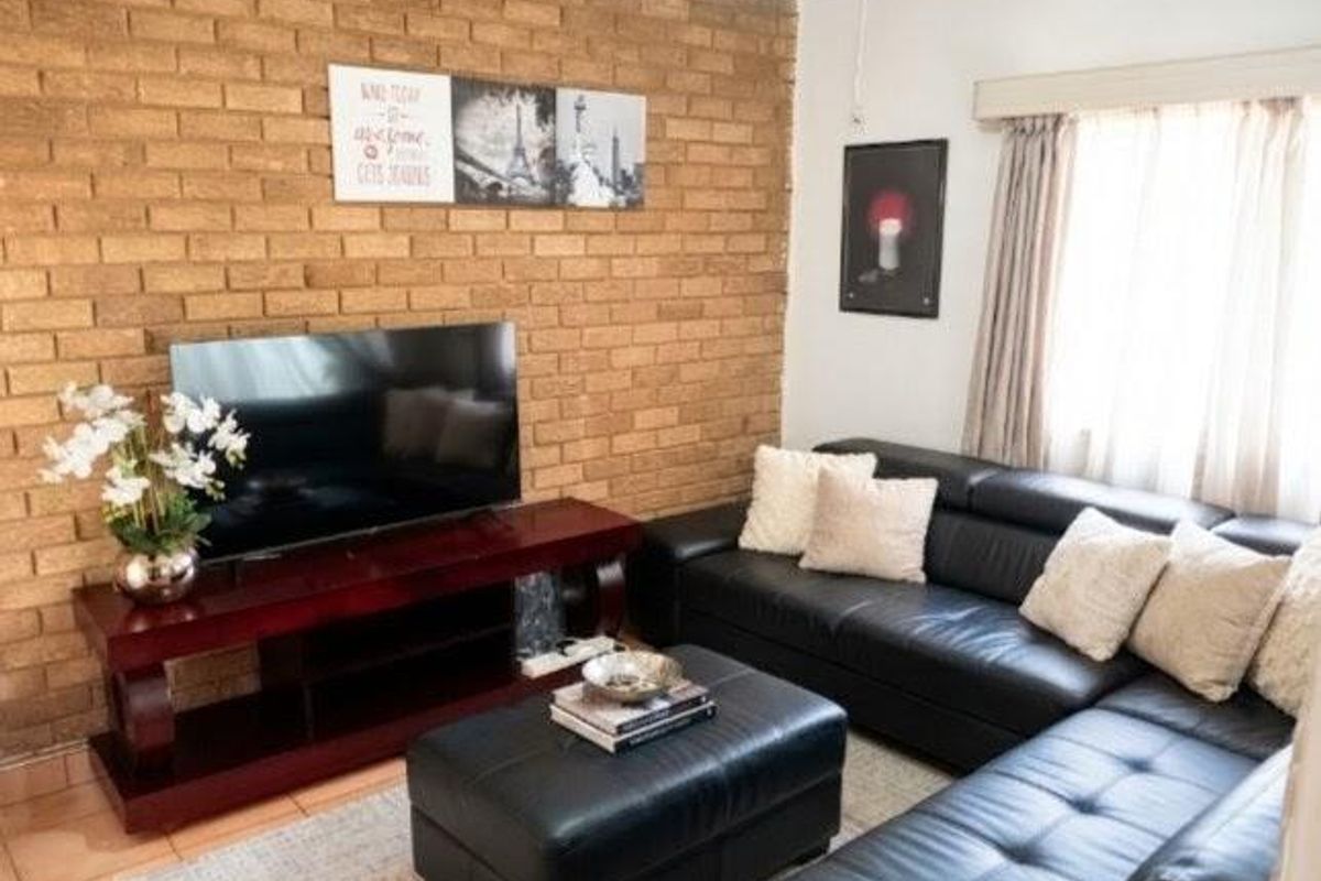 A cozy living room featuring a prominent exposed brick feature wall, tiled flooring, and natural light through window treatments.