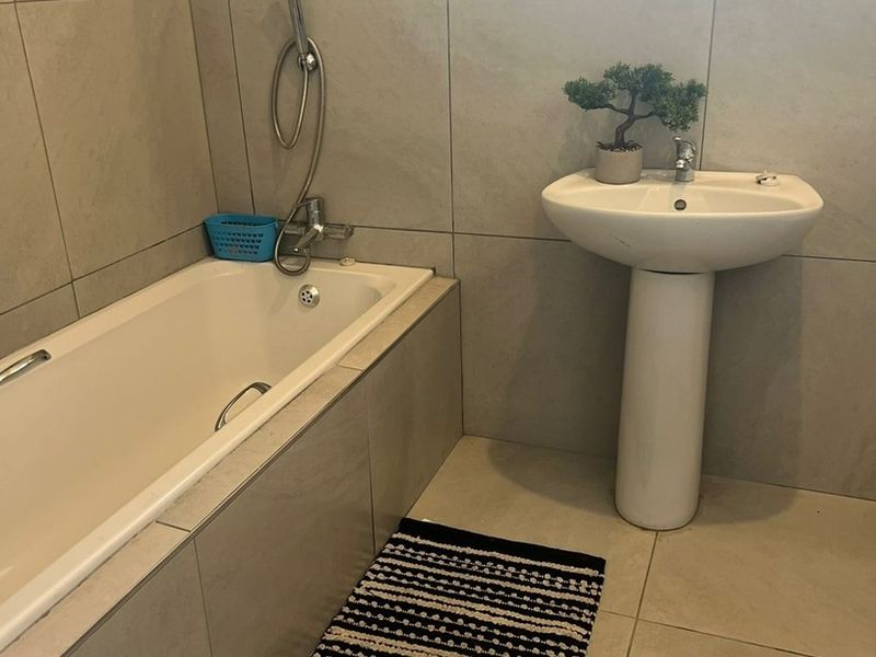 A clean bathroom featuring a pedestal basin, a built-in bathtub with a handheld shower mixer, and neutral wall and floor tiling.