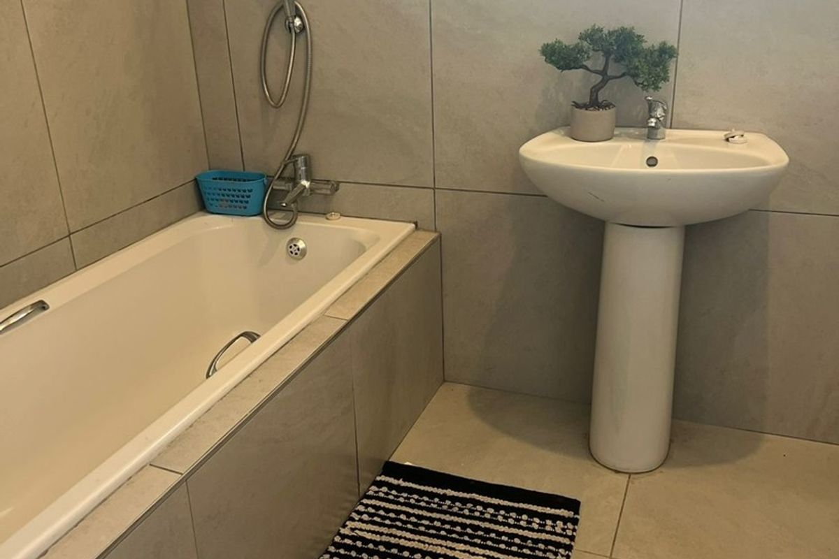 A clean bathroom featuring a pedestal basin, a built-in bathtub with a handheld shower mixer, and neutral wall and floor tiling.