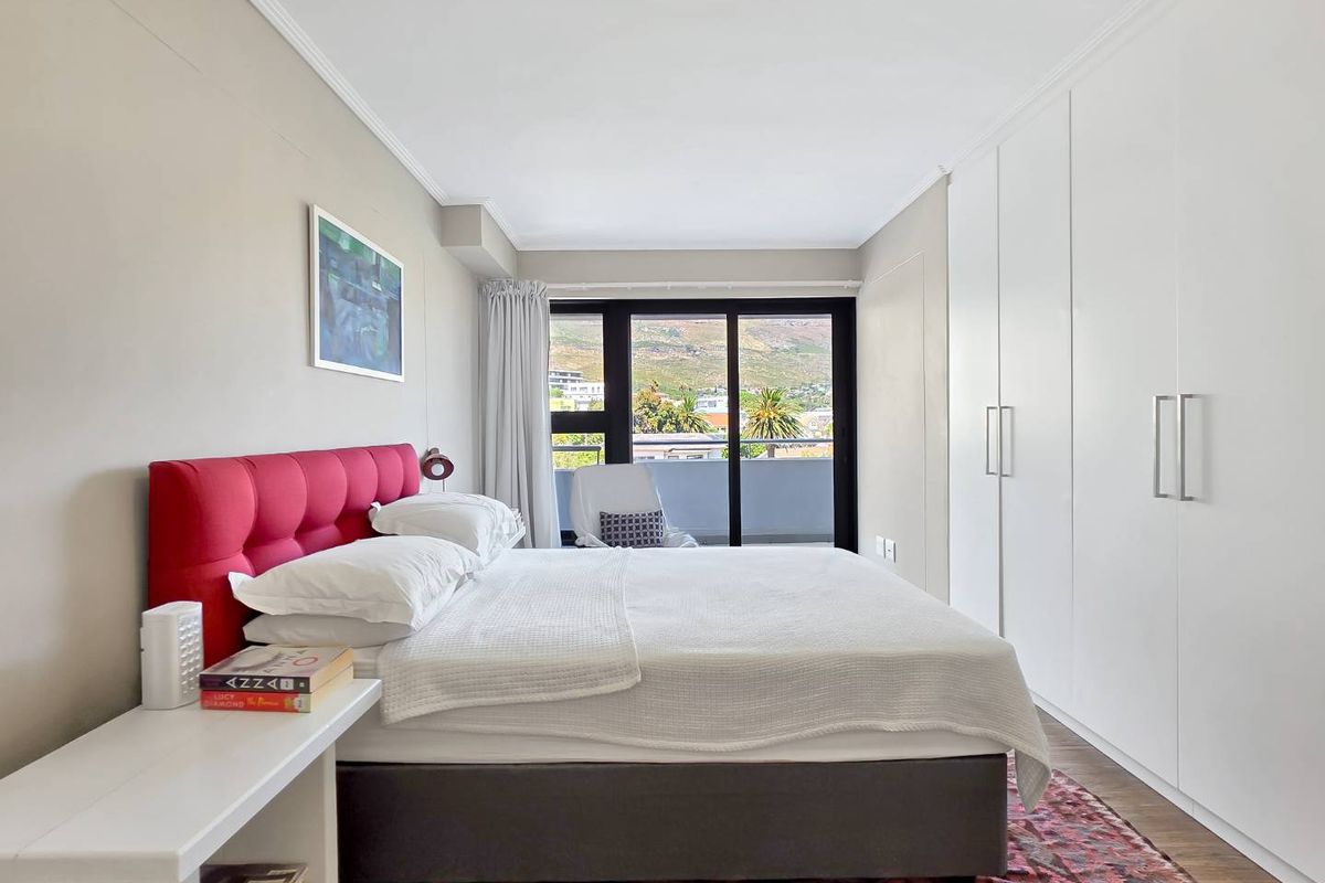 A bright bedroom featuring built-in cupboards, laminate flooring, and a sliding glass door leading to a balcony with scenic views.