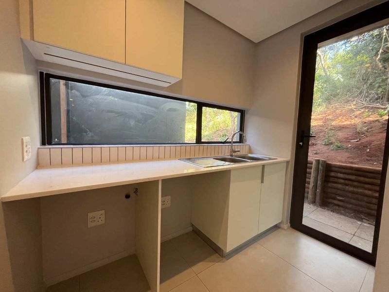 A modern, clean scullery featuring built-in cabinetry, stone countertops, a stainless steel sink, and direct access to the outdoor area.