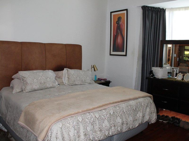 A comfortable bedroom featuring hardwood flooring and a large window with curtain treatments.