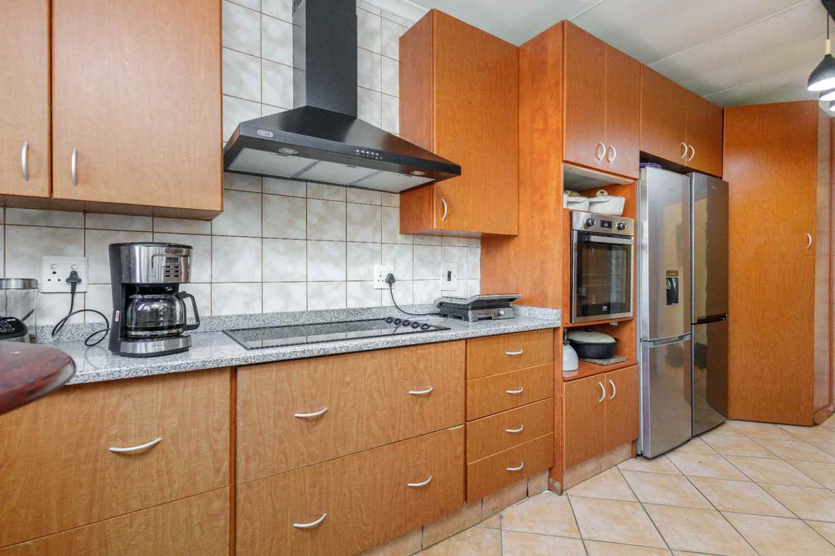 A functional kitchen featuring wooden cabinetry, granite countertops, a built-in oven, and a modern extractor fan with tiled flooring.
