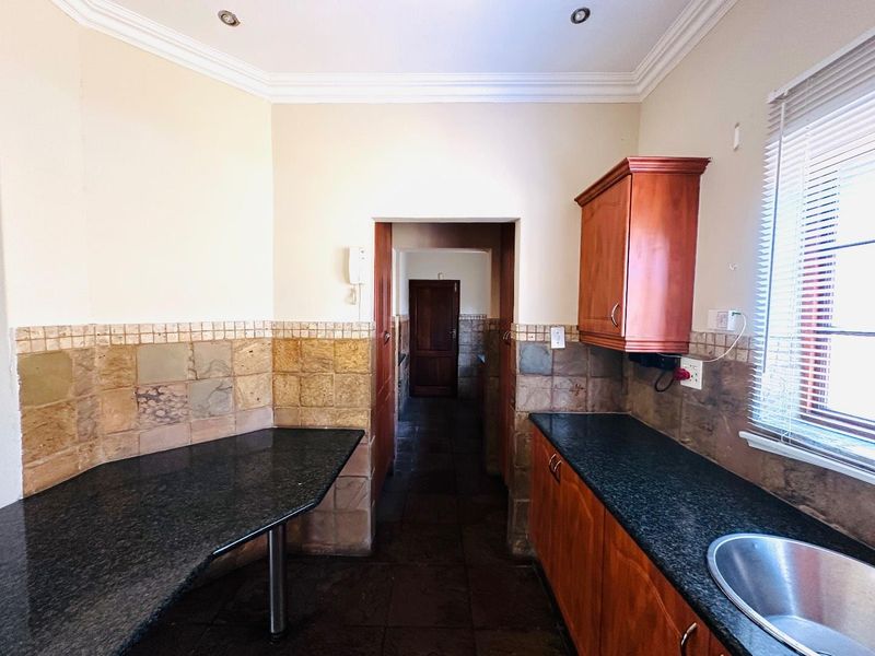 A functional kitchen featuring granite countertops, wooden cabinetry, and stone tile backsplash, offering a practical layout with direct access to the hallway.
