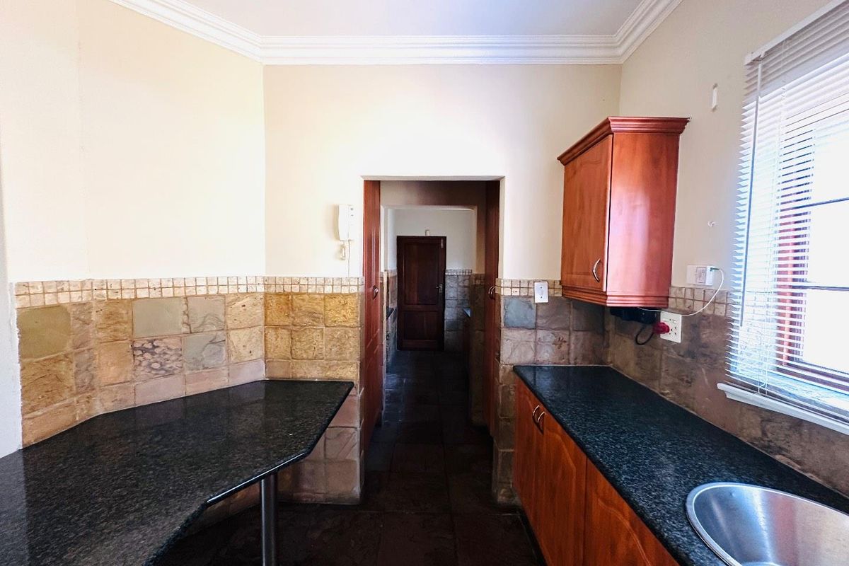 A functional kitchen featuring granite countertops, wooden cabinetry, and stone tile backsplash, offering a practical layout with direct access to the hallway.