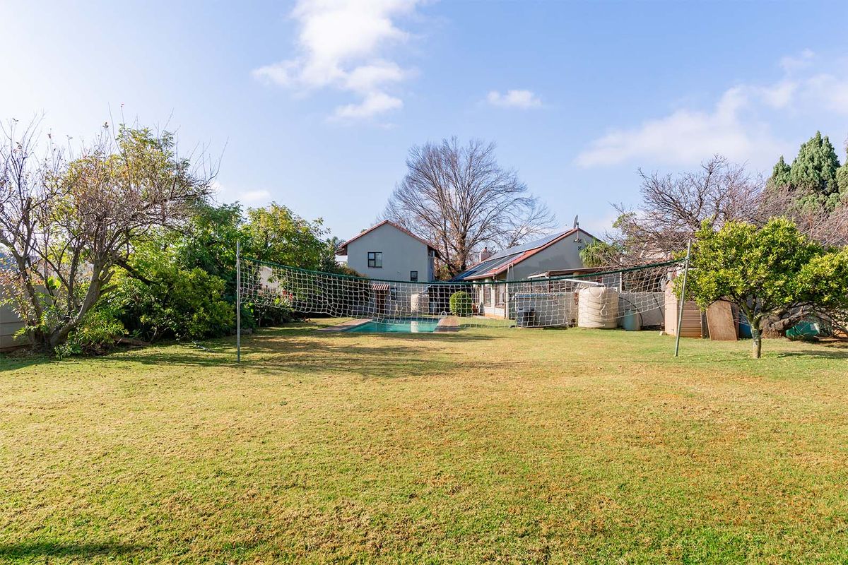 Spacious rear garden featuring a swimming pool, established trees, and a large lawn area, providing a private outdoor space for recreation.