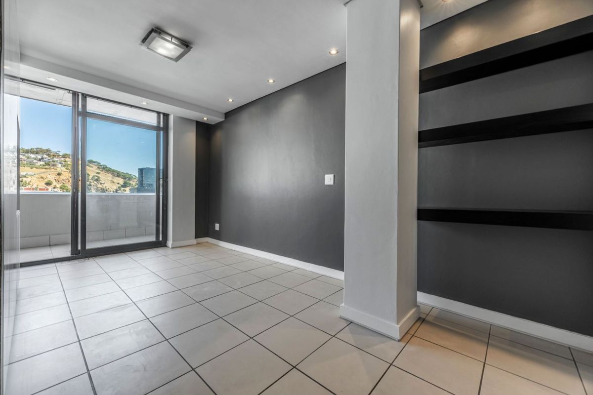 An empty, modern living area featuring tiled floors, built-in shelving, and a large sliding glass door leading to a balcony with scenic views.