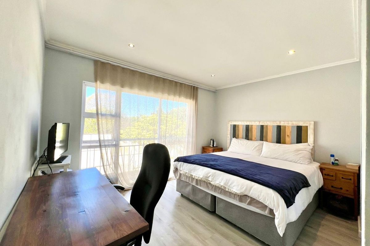 A bright and spacious bedroom featuring light wood-look flooring, recessed ceiling lighting, and a large window with access to a private balcony.